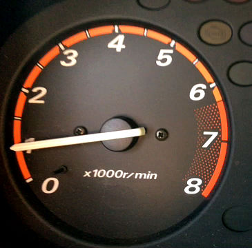 When slowing in a manual car with a gas engine, brake until the the tachometer drops to 1,000rpm and then push in the clutch and come to a complete stop.